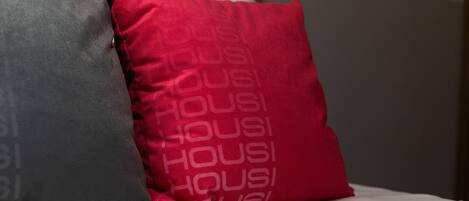 A bed with two pillows, one red and one grey, with the word 'HOUSI' printed on them.