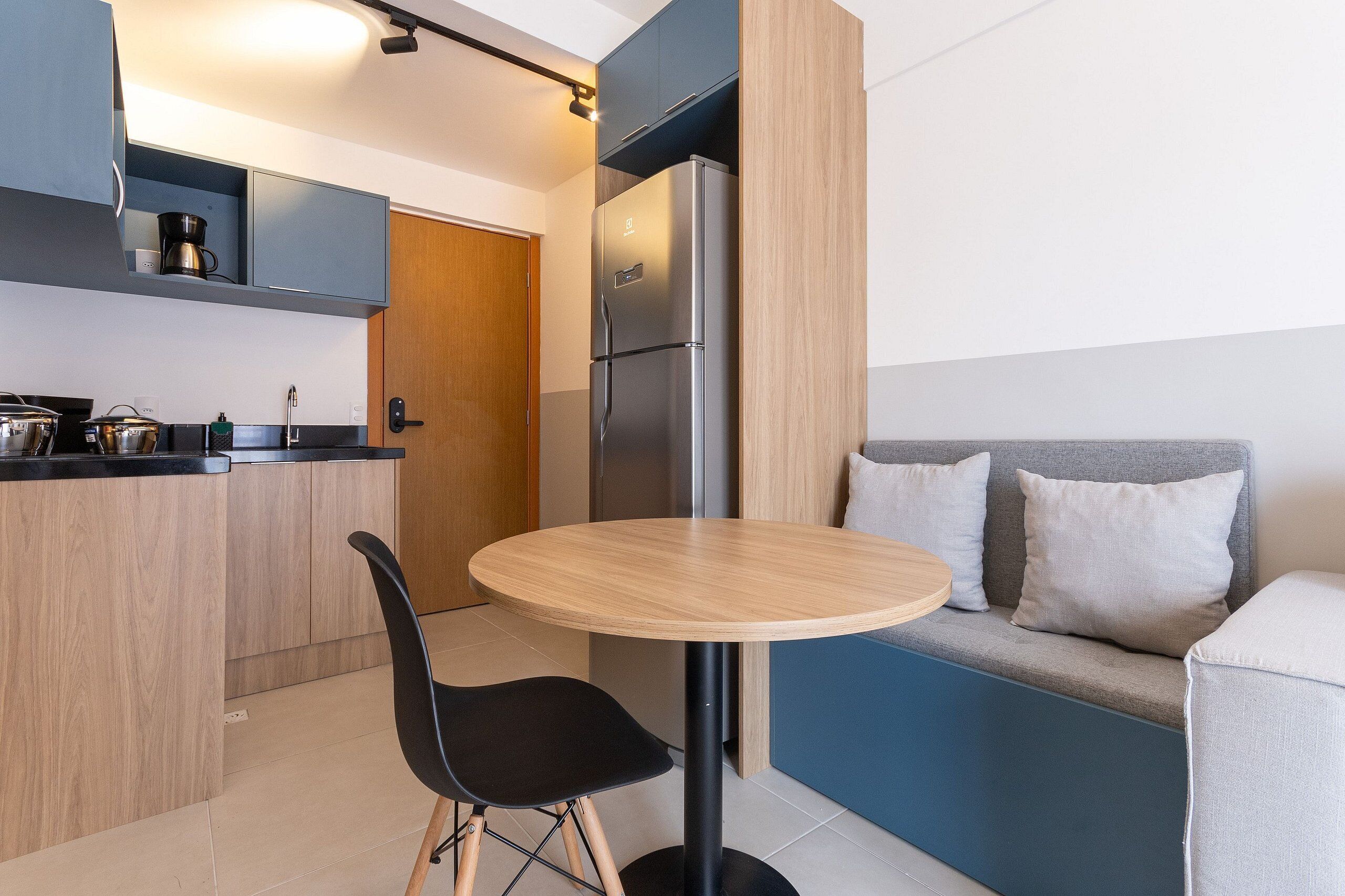 A compact kitchen with a refrigerator, a coffee maker, and a sink. There's a round table with a chair in the center.