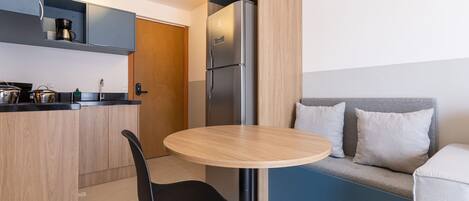 A compact kitchen with a refrigerator, a coffee maker, and a sink. There's a round table with a chair in the center.
