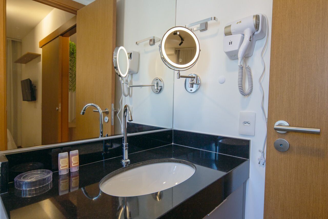 A bathroom with a black countertop, a sink, a mirror, a hairdryer, and a telephone.
