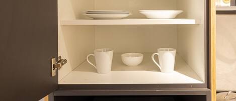 A kitchen with a microwave, shelves with glassware, bowls, and a coffee maker.