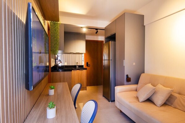 A modern kitchen with a built-in refrigerator, a dining table with chairs, and a sofa in a living area.