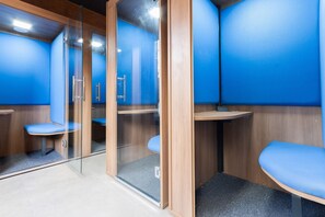 A modern bathroom with glass partitions, blue walls, and wooden benches.