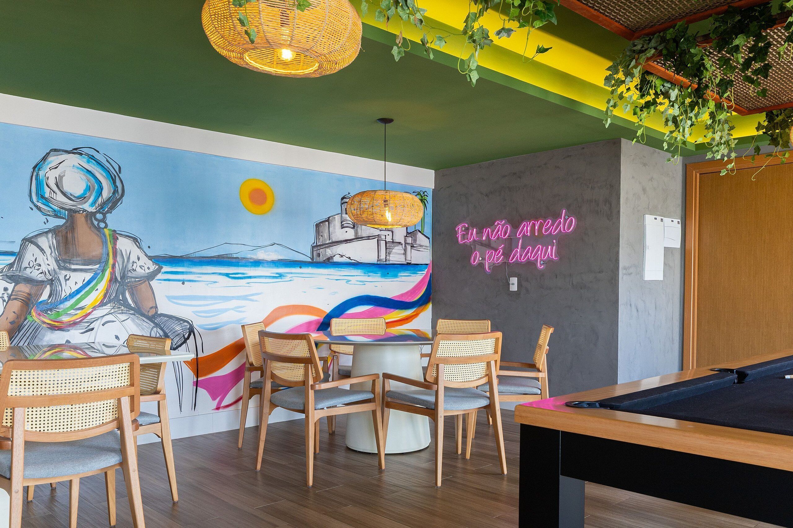 Una mesa de billar, sillas, un mural y un letrero de neón en una habitación con piso de madera y paredes verdes.