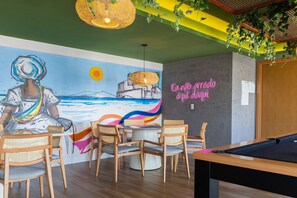 A pool table, chairs, a mural, and a neon sign in a room with wooden flooring and green walls. - Porto Privilege Housi by Carpediem (Salvador)