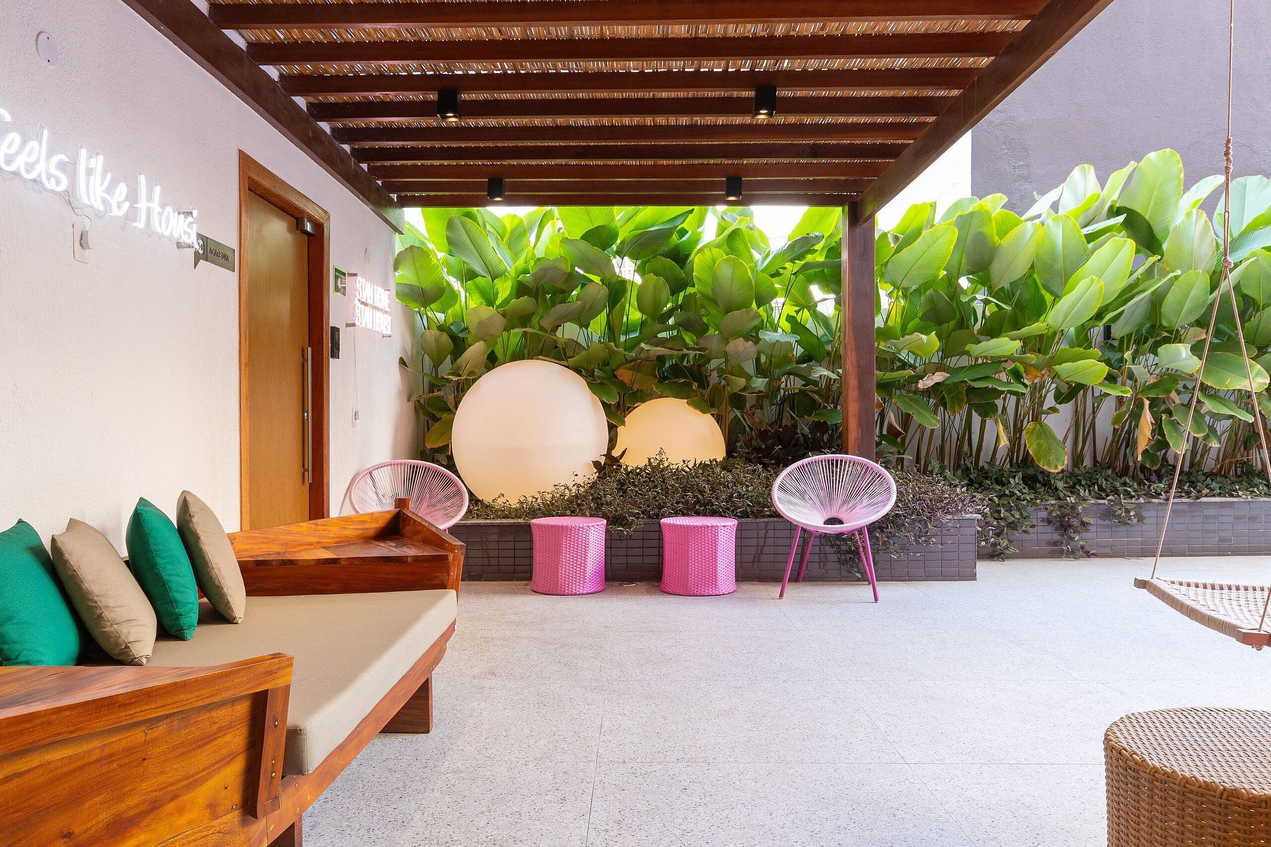 A covered outdoor seating area with a wooden bench, two wicker chairs, and a hanging chair.