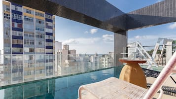 Una piscina en la azotea con vistas despejadas del paisaje urbano, una silla de descanso y un edificio moderno al fondo.