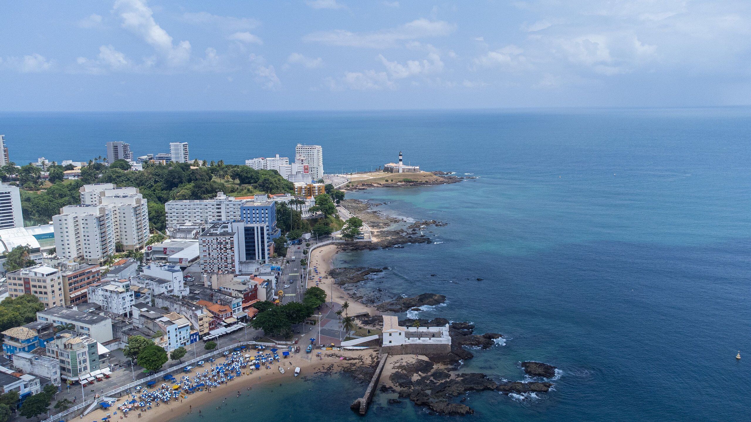 An aerial view of a coastal city with high-rise buildings, a beach, and rocky coastline.