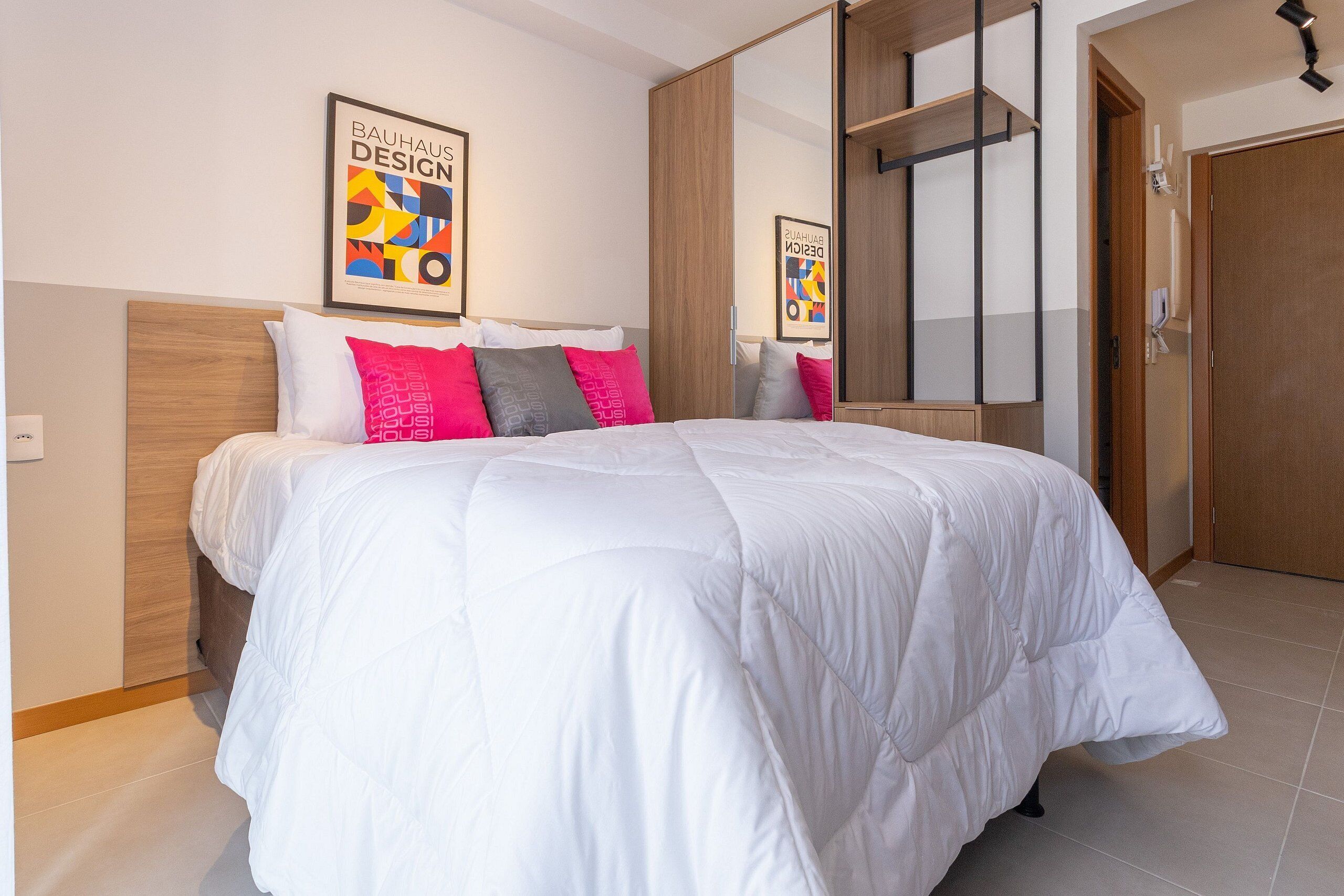 A bedroom with a bed, pillows, a wooden headboard, a large mirror, and a wardrobe.