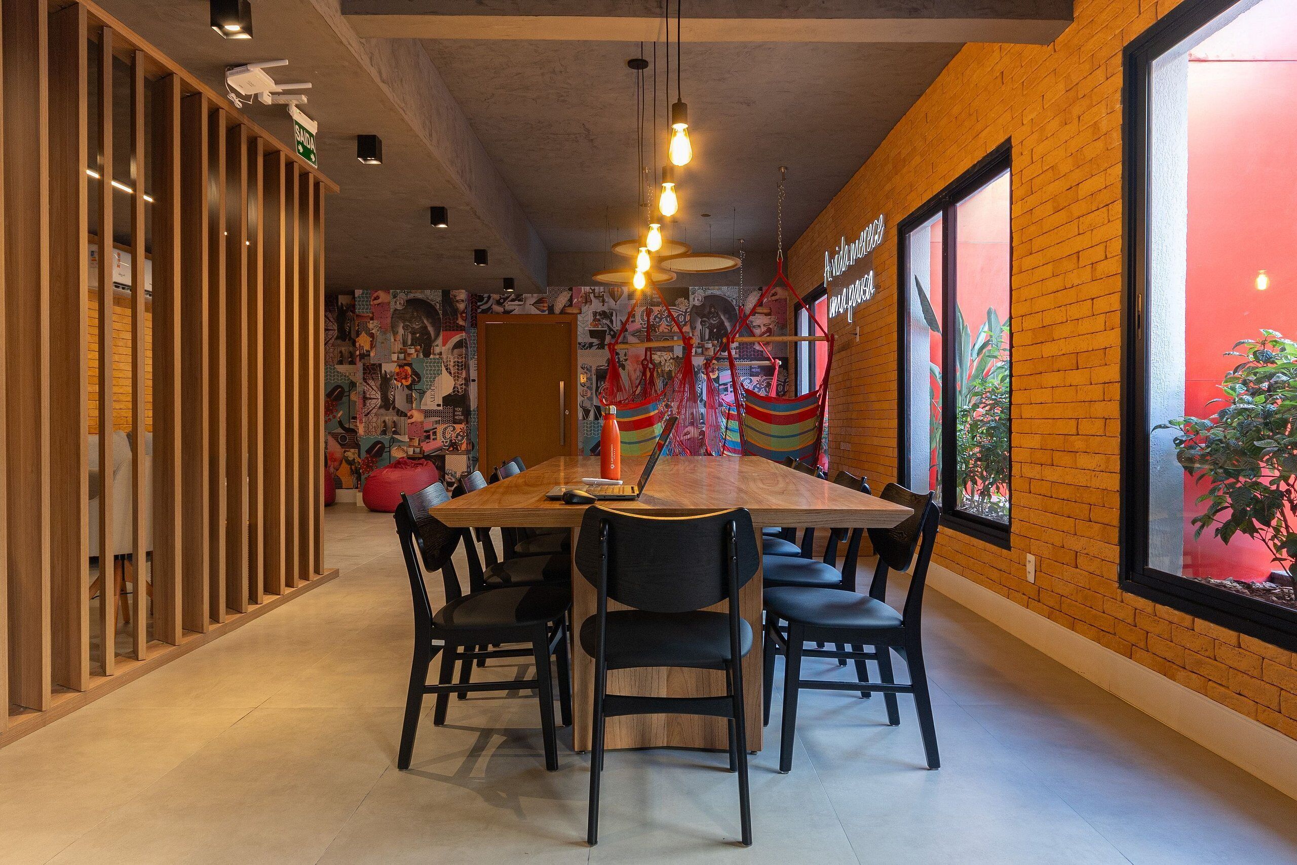 A modern dining area with a long wooden table, black chairs, and a colorful mural on the wall.