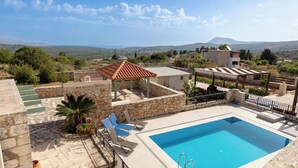 Une piscine sur le toit offrant une vue dégagée sur le paysage environnant, des murs en pierre et quelques chaises longues.