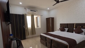Une chambre dotée d’un grand lit, d’un ventilateur de plafond, d’un appareil de climatisation, d’une armoire et d’une petite table avec une bouilloire.