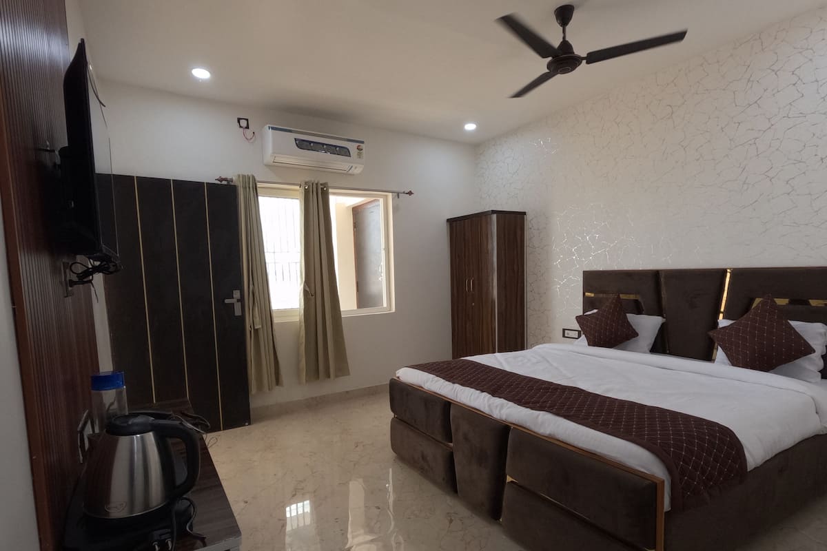 A bedroom with a large bed, a ceiling fan, an air conditioning unit, a wardrobe, and a small table with a kettle.