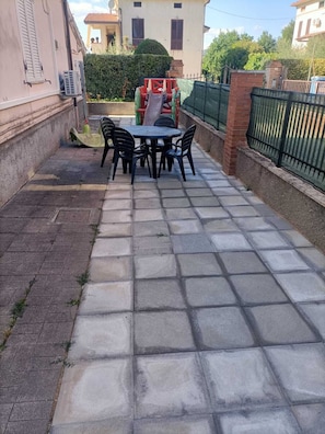 A paved patio with a table and chairs, a small play structure, and a brick wall.