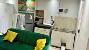 A compact living space with a green sofa, a refrigerator, a microwave, a sink, and a cabinet with animal designs. - Mowetu Guest House (Cape Town)