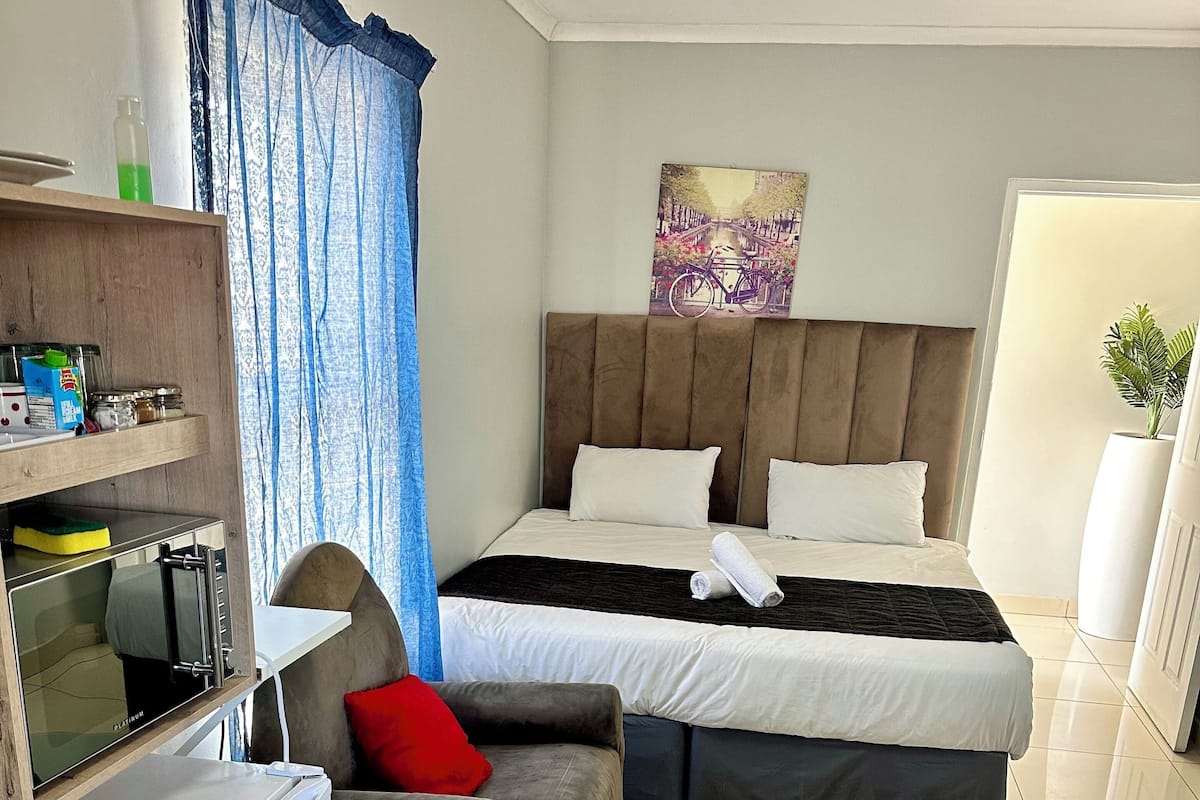 Ein Hotelzimmer mit Bett, einer kleinen Küchenzeile, einer Sitzecke mit Sofa und Sessel sowie einem großen Fenster mit Vorhängen.