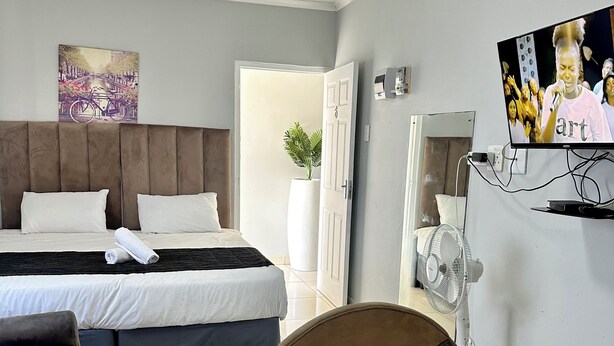 A hotel room with a bed, a TV, a fan, and a painting on the wall. - Mowetu Guest House (Cape Town)