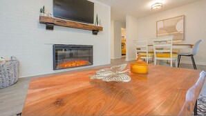 A modern living room with a fireplace, a wooden coffee table, and a dining area with chairs and a table. - The Beehive New 4 Bedroom Listing Next to CNU (Newport News)