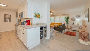 A modern kitchen with white cabinets, a built-in oven, and a coffee maker. There is a dining area with a sofa and a small Christmas tree. - The Beehive New 4 Bedroom Listing Next to CNU (Newport News)