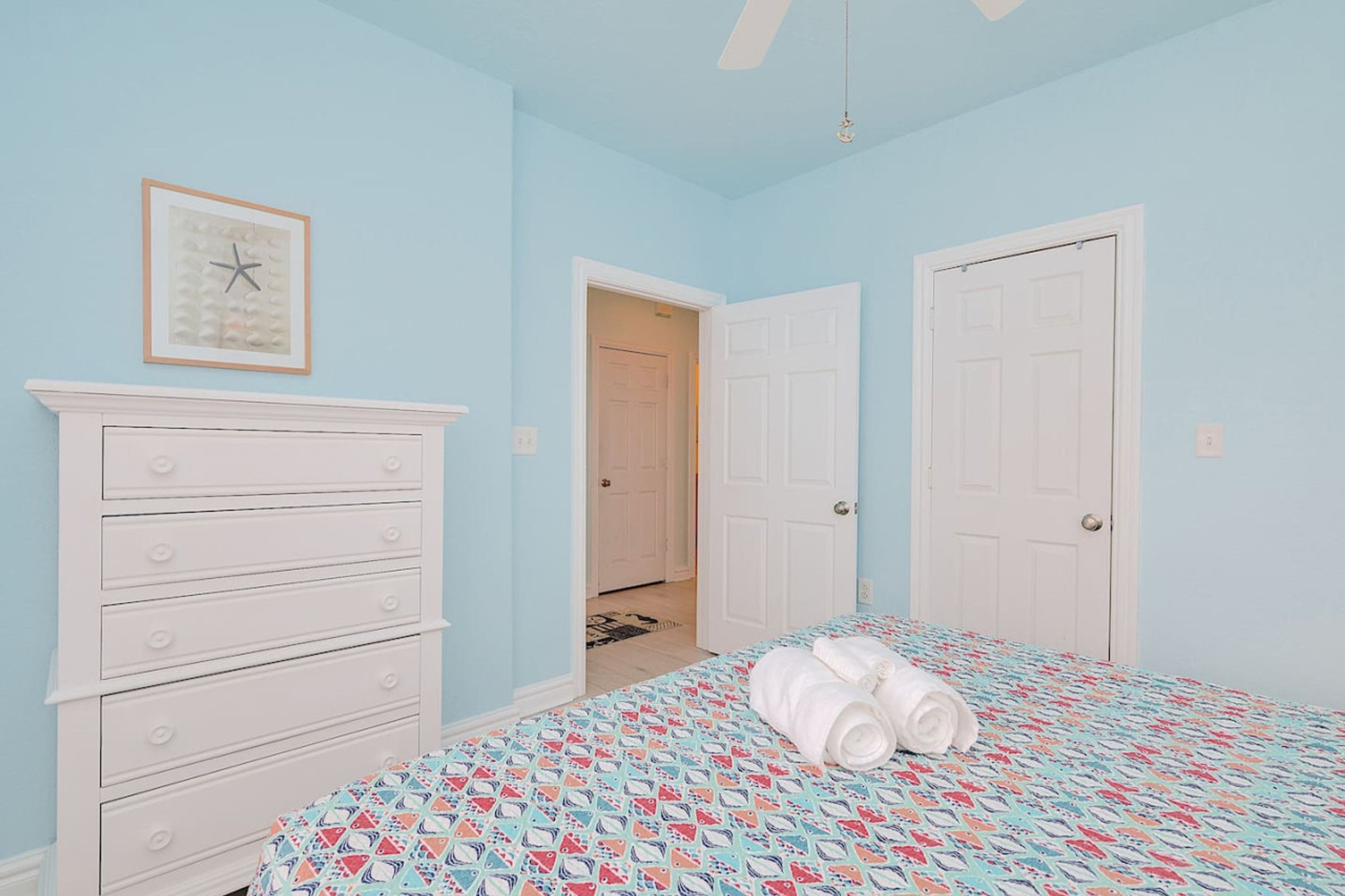 A bedroom with a bed, a dresser, a door, and a hallway.
