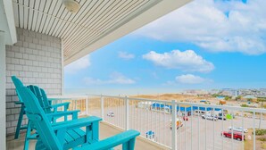 A balcony with turquoise Adirondack chairs, a white railing, and a view of a parking lot and distant buildings. - 4BR Waterfront Penthouse Pool Views (Virginia Beach)