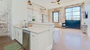 A spacious kitchen with a large island, white cabinetry, and a brick accent wall. - Ice Ice Baby Downtown Newport News (Newport News)
