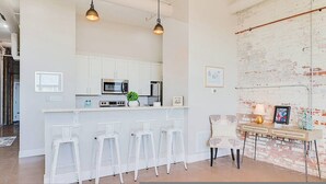 A modern kitchen with white cabinets, a central island with bar stools, a microwave, and a refrigerator. - Ice Ice Baby Downtown Newport News (Newport News)