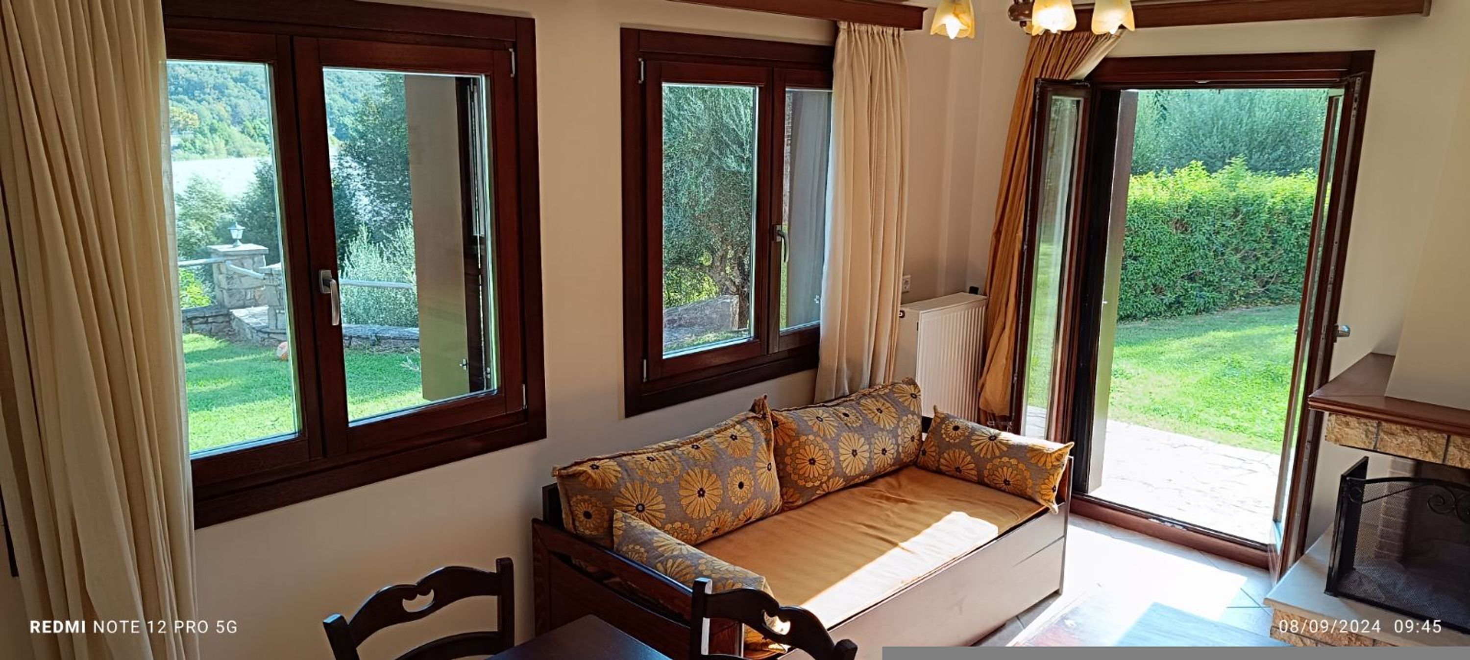 Ein gemütliches Zimmer mit einer Couch, einem Kamin und großen Fenstern mit Blick auf einen Garten.