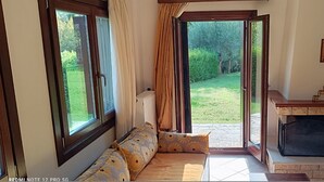 A cozy room with a sofa, a fireplace, and a view of the garden. - Evinos Village Resort (Nafpaktos)