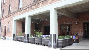 A building with a brick facade, a covered entrance with columns, and planters along the walkway. - The Speakeasy Downtown Newport News (Newport News)