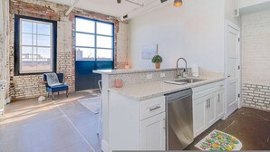 A modern kitchen with a large island, a dishwasher, and a window with a city view. - The Speakeasy Downtown Newport News (Newport News)