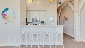 A kitchen with white cabinets, a microwave, and a bar area with white stools. - The Speakeasy Downtown Newport News (Newport News)