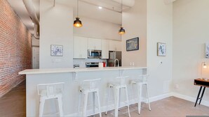 A modern kitchen with white cabinets, stainless steel appliances, and a central island with bar stools. - The Safe House Downtown Newport News (Newport News)