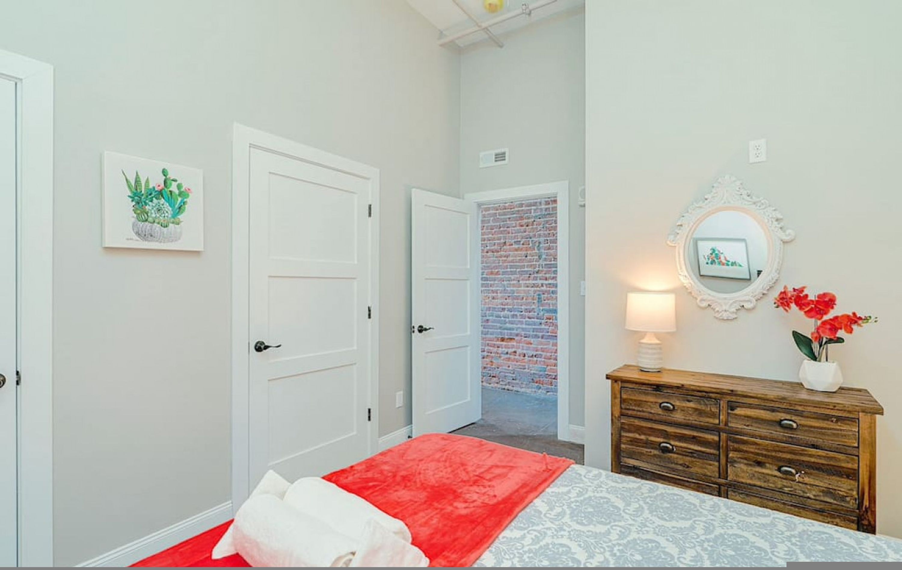 Ein Schlafzimmer mit Bett, Schminktisch, Spiegel, Tür und einer Ziegelwand.