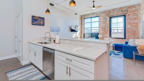 A modern kitchen with white cabinets, a granite countertop, and a large window. - The Safe House Downtown Newport News (Newport News)