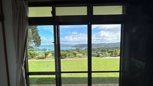 A room with a large sliding glass door leading to an outdoor deck with a view of a green landscape and a body of water. - Ocean View House Nakijin (Nakijin)