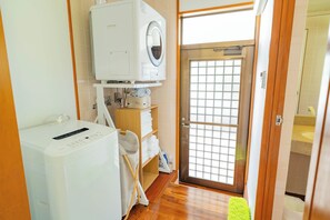 A laundry room with a washing machine, a drying rack, and a shelf with folded towels.