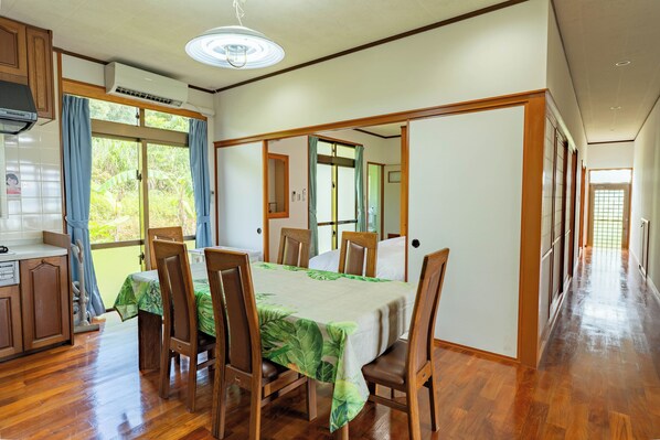 A dining area with a table set for six, wooden chairs, and a view of the outdoors through a sliding door. - Ocean View House Nakijin (Nakijin)
