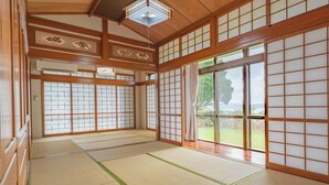 A traditional Japanese room with tatami flooring, sliding doors, and a view of a garden. - Ocean View House Nakijin (Nakijin)