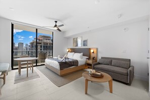 A modern bedroom with a large bed, a sofa, a dining table, and a balcony with a city view.