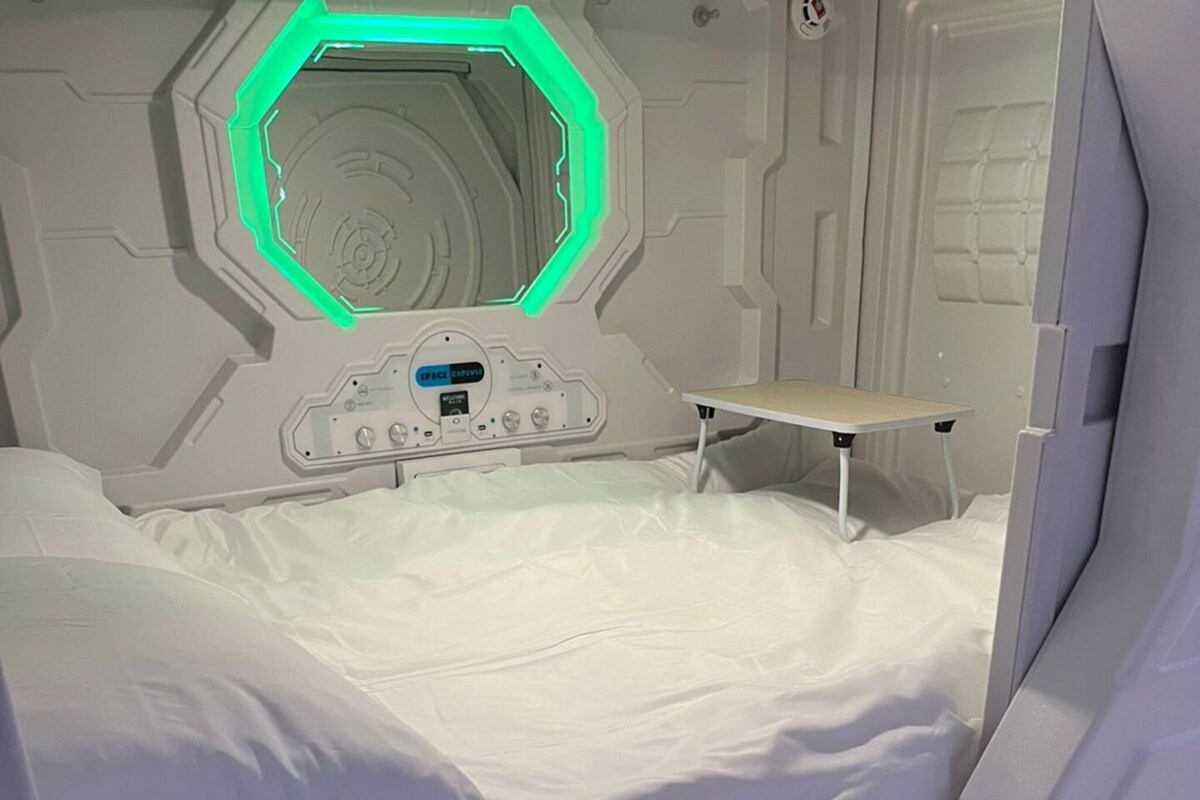A hospital bed with a control panel, a small table, and a green-lit hexagonal window.