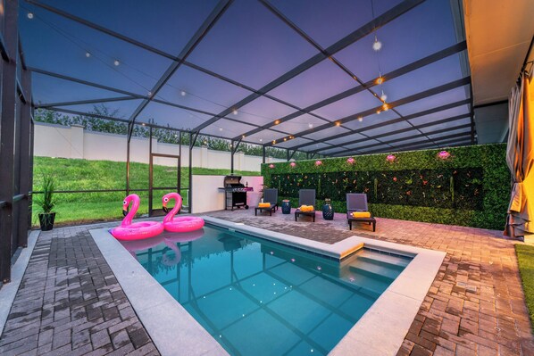 A covered outdoor pool area with a grill, lounge chairs, and a green wall with flowers. - 5BD/4.5BA home, 9 mi. from Disney, Free Access to Lazy River and Waterpark! (Kissimmee)