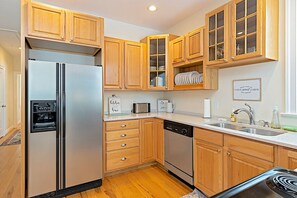 Eine Küche mit Holzausstattung, einem Edelstahl-Kühlschrank, einer Spülmaschine und einer Mikrowelle.