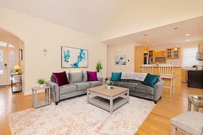 Ein geräumiges Wohnzimmer mit einer grauen Sofagarnitur, einem Couchtisch und einer Küchenzeile im Hintergrund.