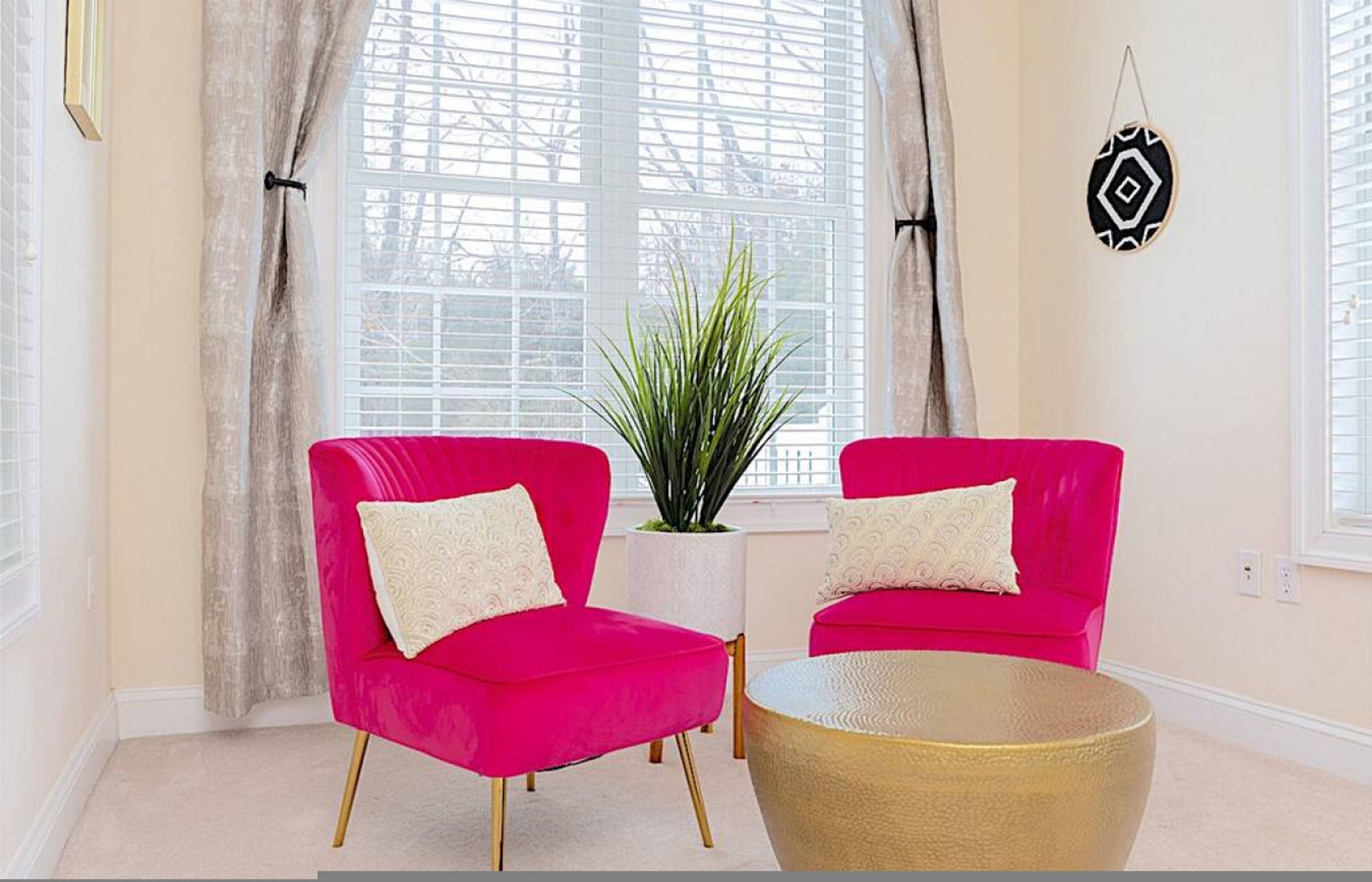 Una habitación con dos sillas de color rosa brillante, una mesa redonda dorada y una planta en maceta.