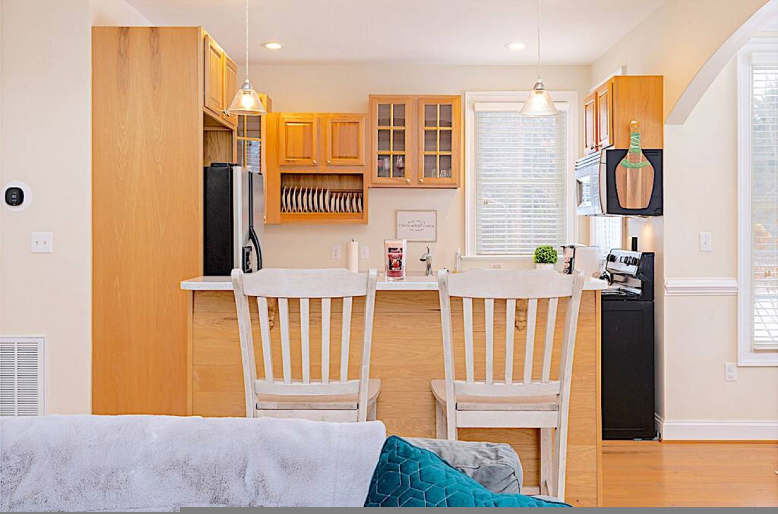 A compact kitchen with wooden cabinets, a black refrigerator, and a dining area with two white chairs.