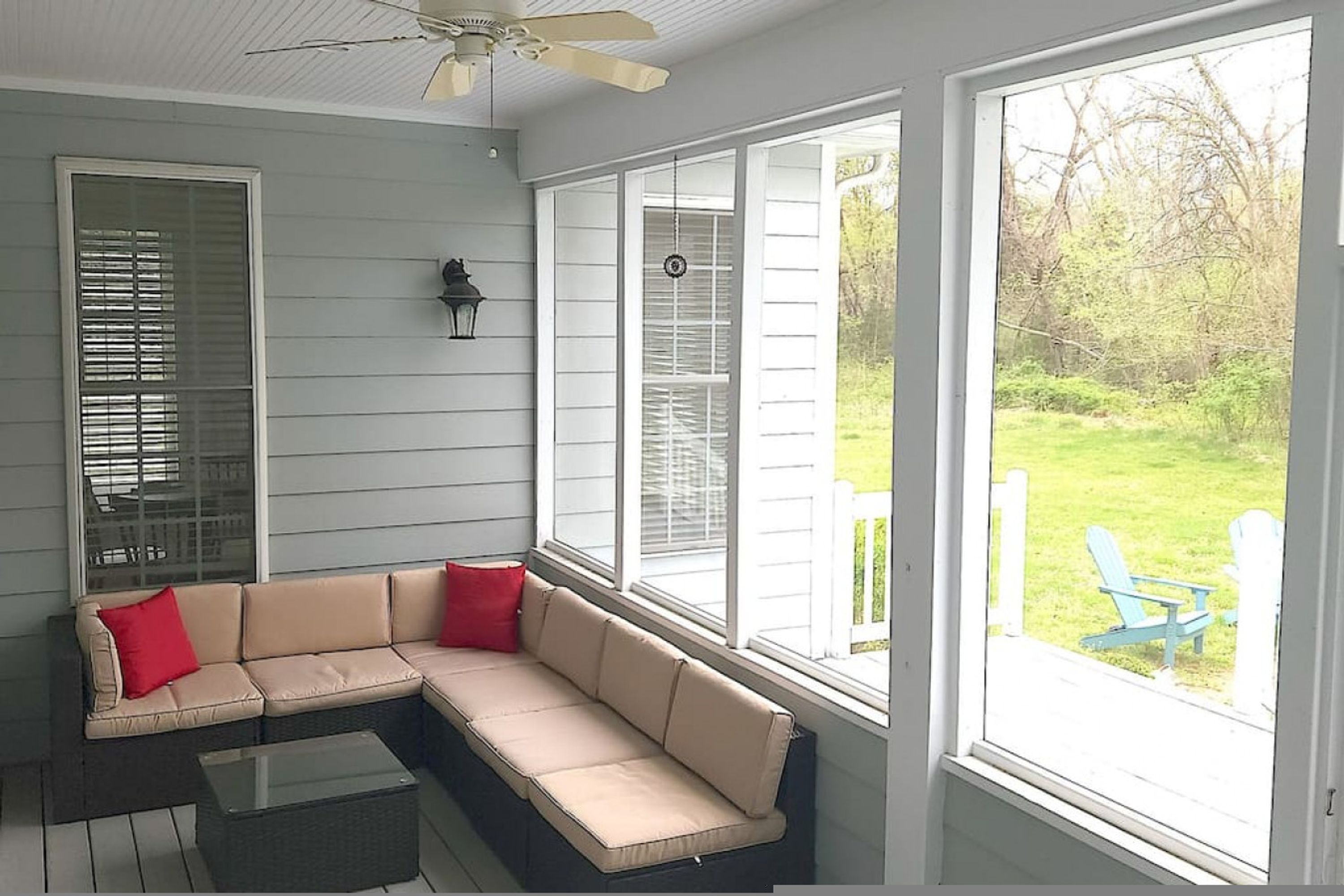 A covered porch with a beige sectional sofa, a glass coffee table, and a view of a grassy yard.