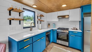 Een moderne keuken met blauwe kastjes, witte aanrechtbladen en roestvrijstalen apparatuur.