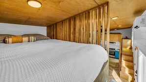 Een compacte slaapkamer met een houten plafond, een bed met een gestreept kussen, en een kitchenette.