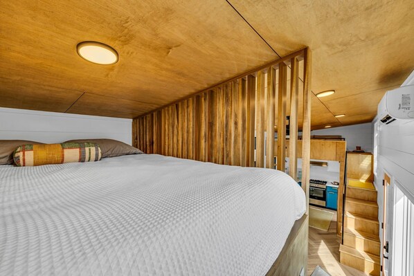 Un dormitorio pequeño con techo de madera, cama con cojín estampado y un área de kitchenette.